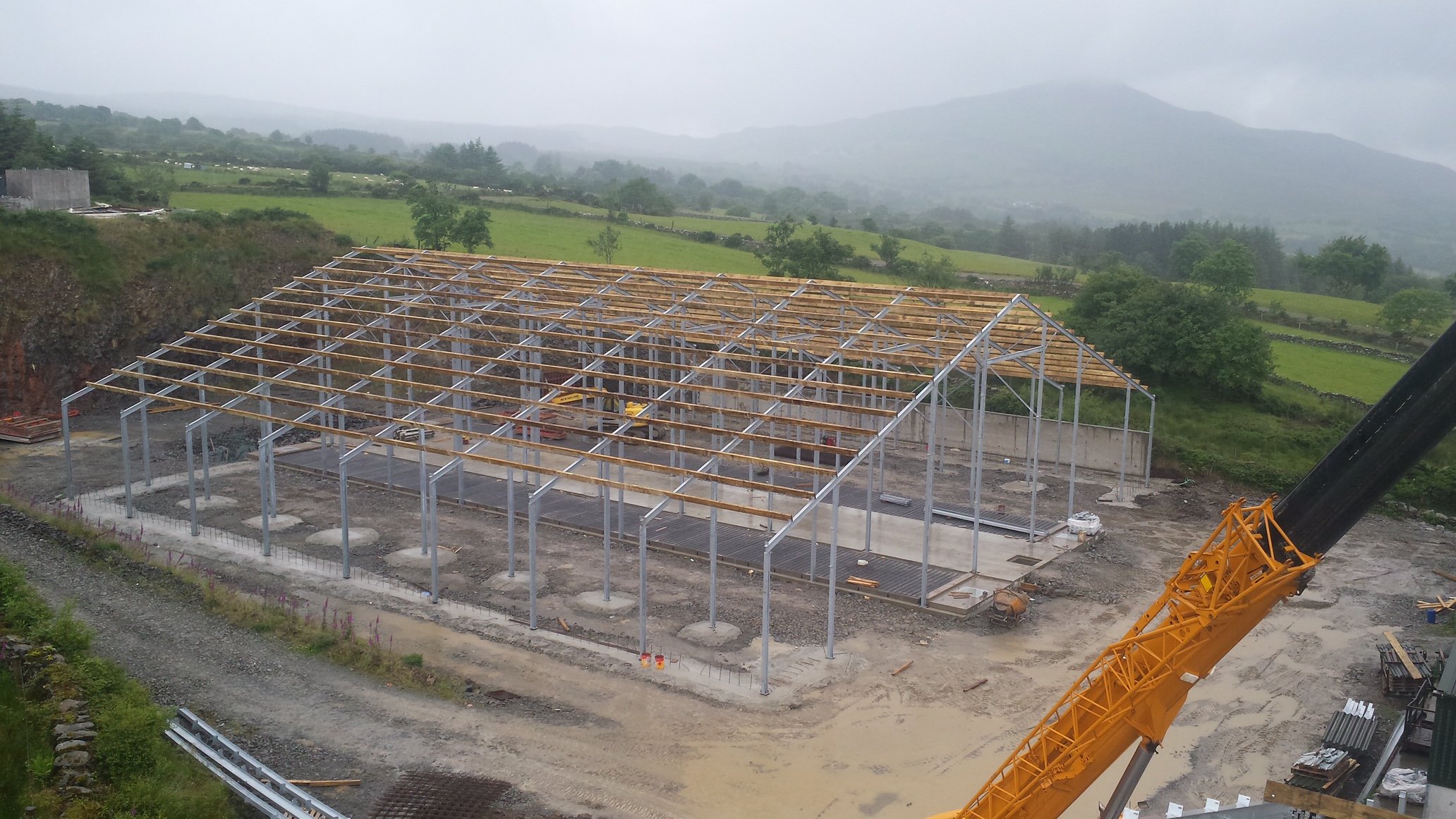 Steel frame going up on a concrete slab in open countryside with a mobile crane alongside and hills behind