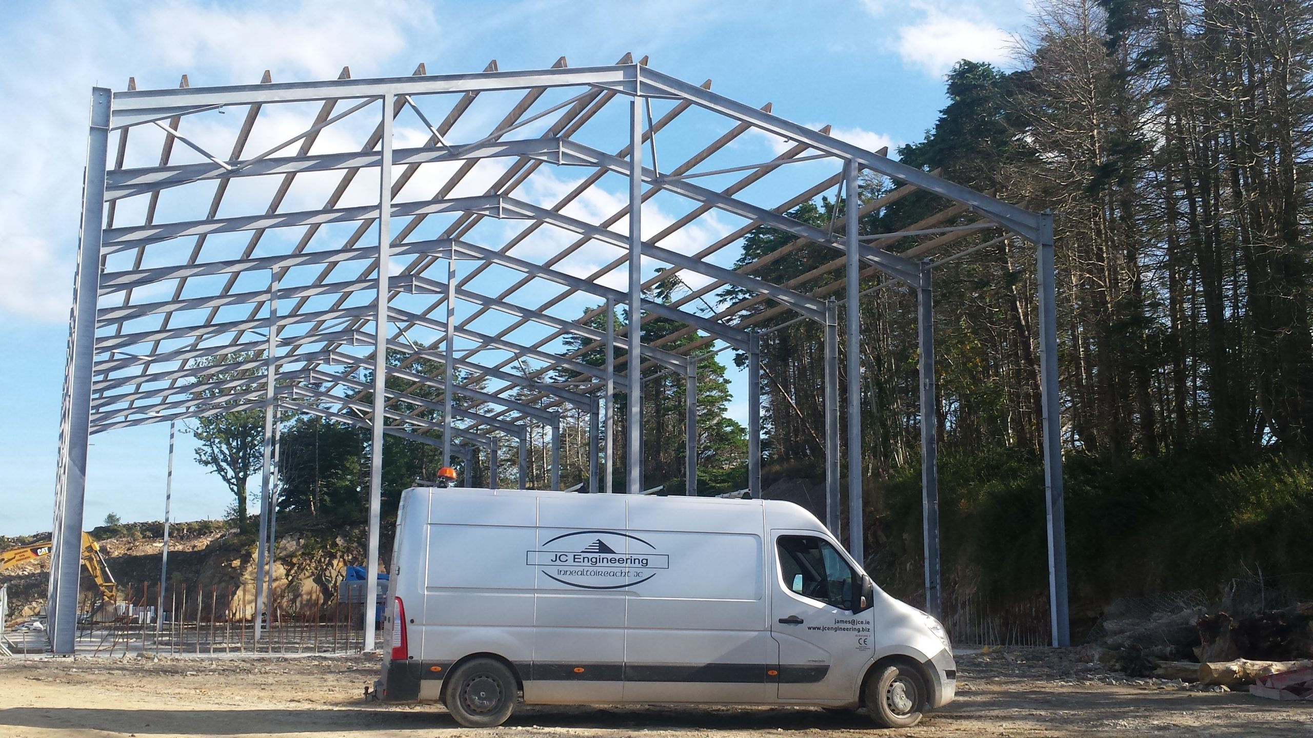 Erected steel portal frame on a site with a van parked in front and a conifer treeline behind