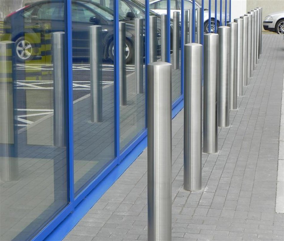 Row of stainless steel bollards on a paved forecourt outside a glazed shopfront
