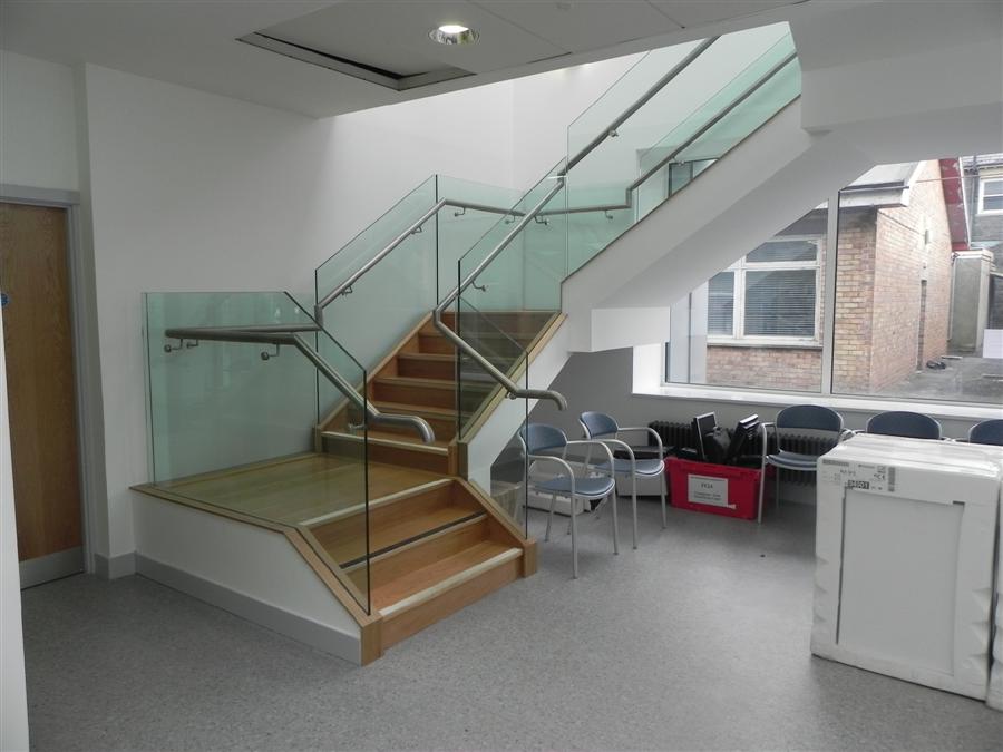 Interior staircase with a glass balustrade and a stainless handrail, timber treads on the lower flight