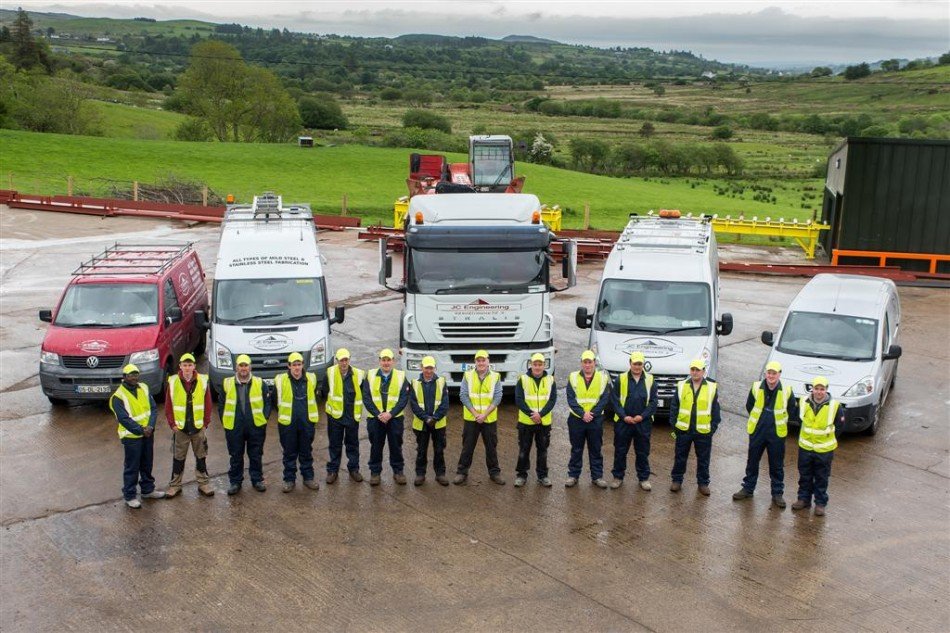 About twenty staff in high-visibility clothing lined up in front of the van and truck fleet, with green hills behind